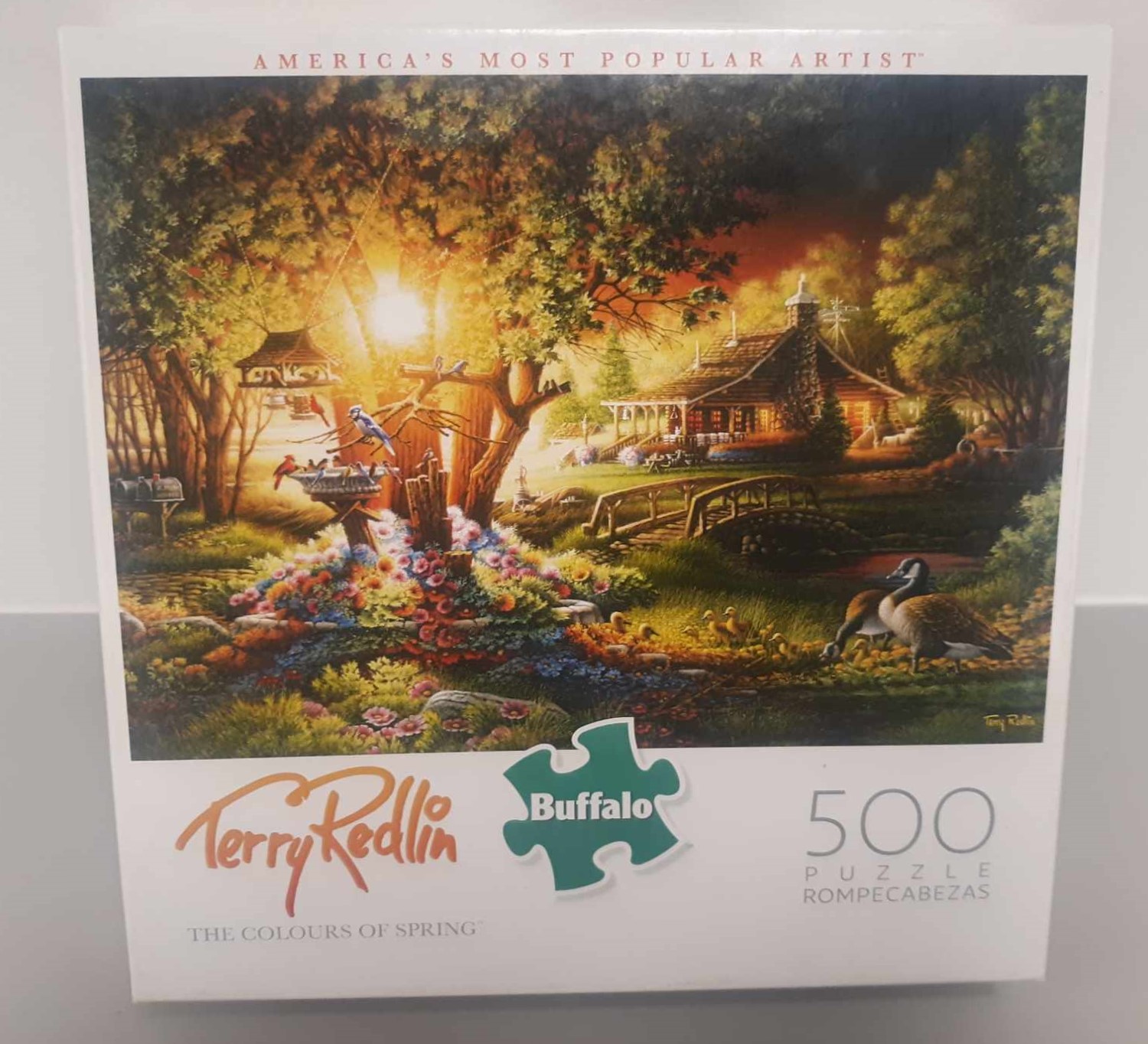 Image of puzzle cover titled "The Colours of Spring" that shows a cabin in the woods next to a giant tree when the sun is going down.