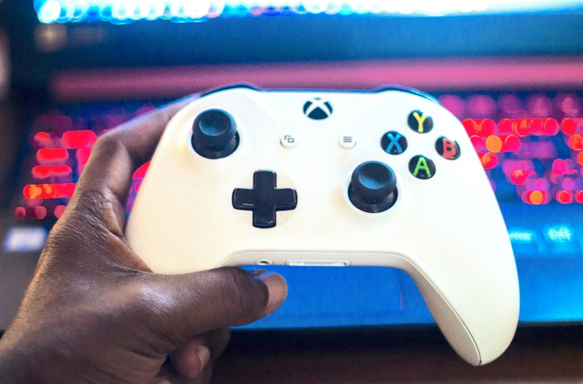 A hand holding a gaming controler in front of a computer keyboard.