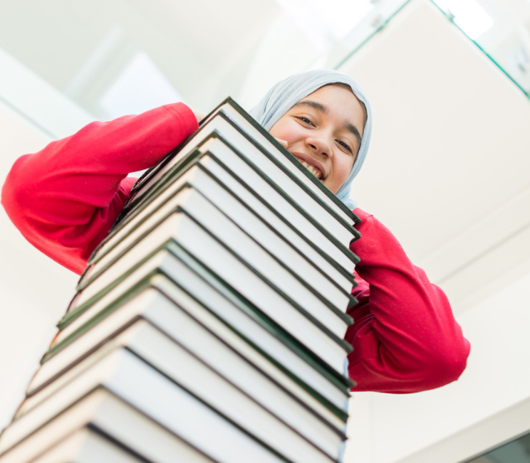 Teen looking over a stack of books.