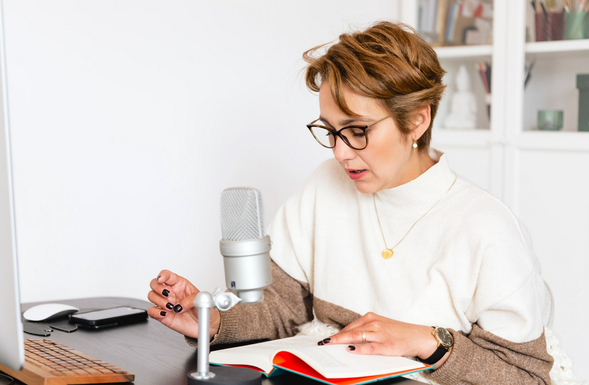 Woman sitting in front of a microphone reading from a book.