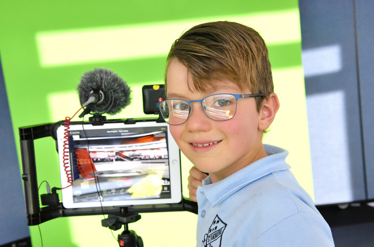 A young boy with a video camera set up in front of a green screen.