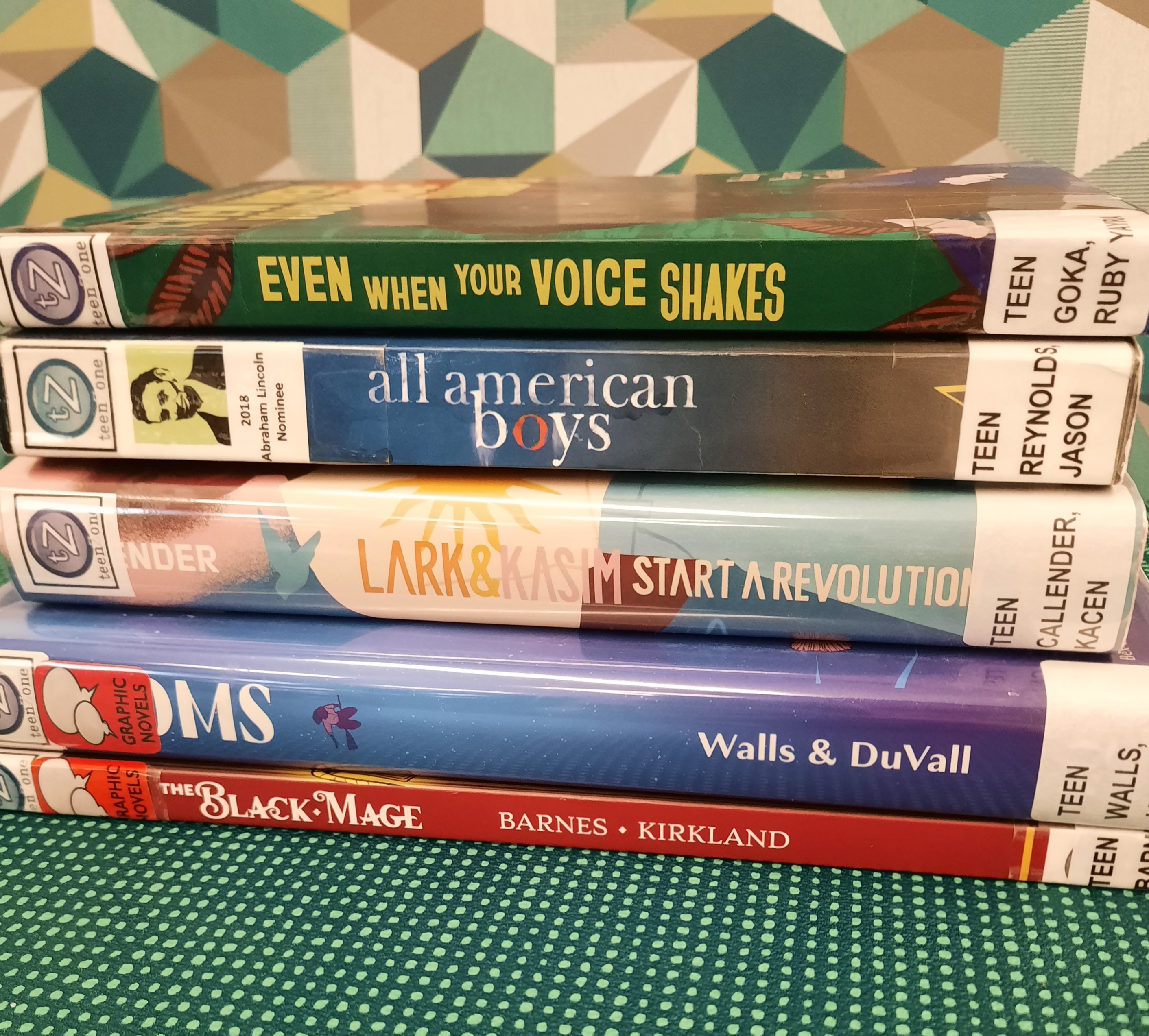 Book stack showing the following books: "The Black Mage," "Brooms" "Lark & Kasim Start a Revolution," "All American Boys," and "Even when your voice shakes"