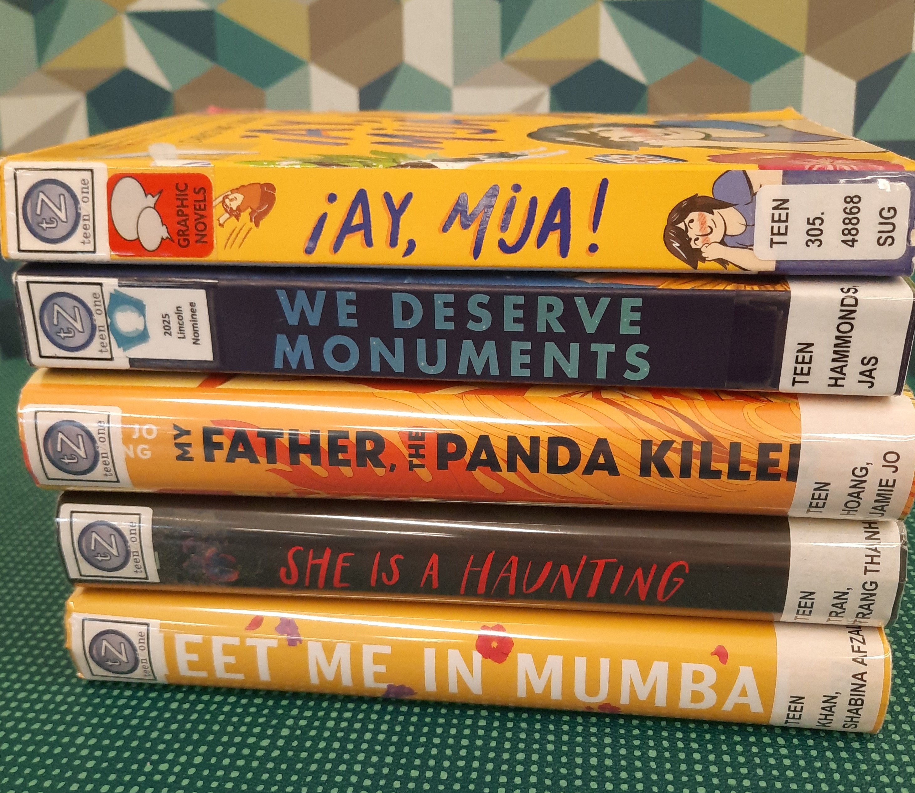 Book Stack showing the following titles: "Ay, Mija," "We Deserve Monuments," "My Father, the Panda Killer," "She is a Haunting," and "Meet me in Mumba"