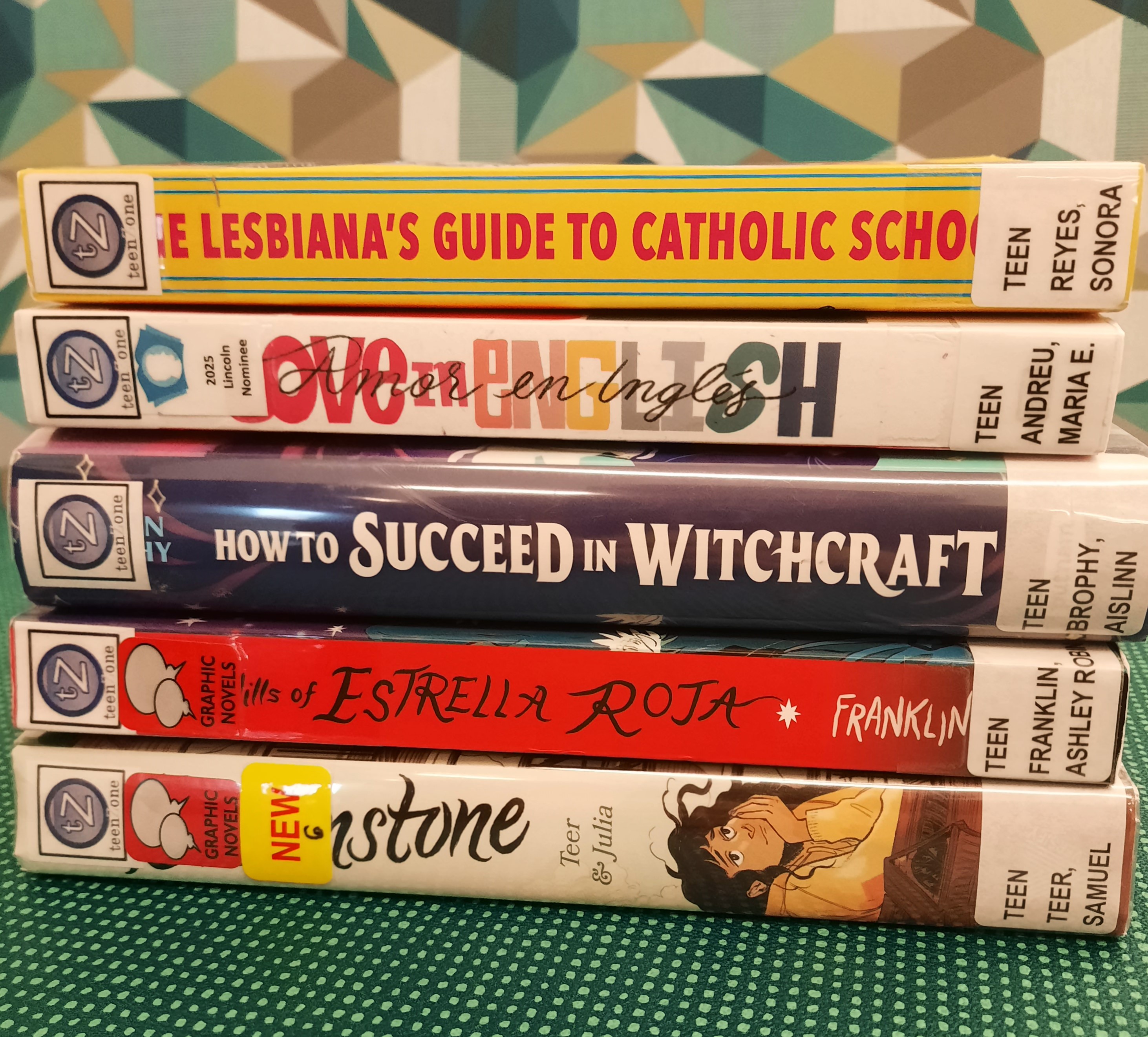 Book Stack showing the following titles: "The Lesbiana's Guide to Catholic School," "Love in English," "How to Succeed in Witchcraft," "The Hills of Estrella Roja" and "Brownstone"