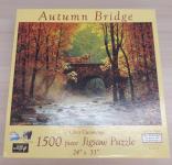 Image of a puzzle cover titled "Autumn Bridge" Showing a river flowing between rows of trees with orange leaves and a stone bridge.