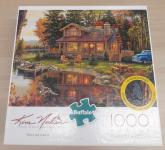 Image of a puzzle cover titled "Peace Like a River" Showing a cabin in the woods next to a river and a blue car.