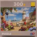 Puzzle cover with an image of chairs sitting by the beach and a light house with boats on the water.